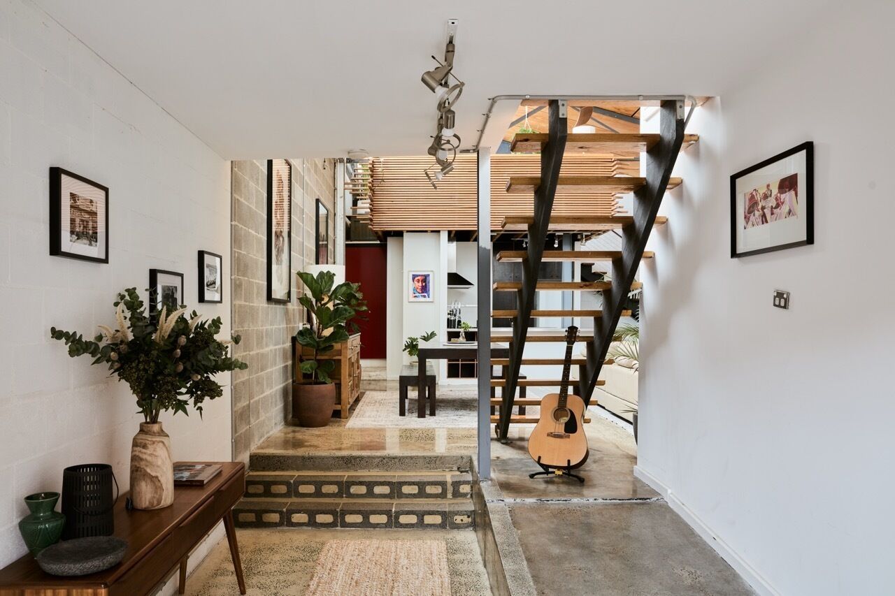 Una escalera que sube a un segundo piso, con una guitarra apoyada en la pared.