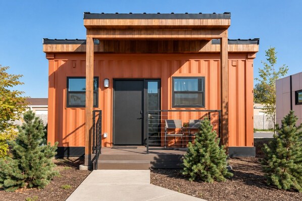 A modern building with a wooden facade, a central entrance with a door, and a small porch area with seating. - Modern Cargo House in Salt Lake City (Salt Lake City)