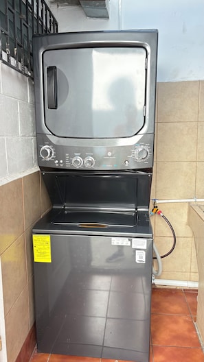 Lavadora compacta y moderna con panel de control, etiqueta amarilla de eficiencia energética y conexión para manguera.