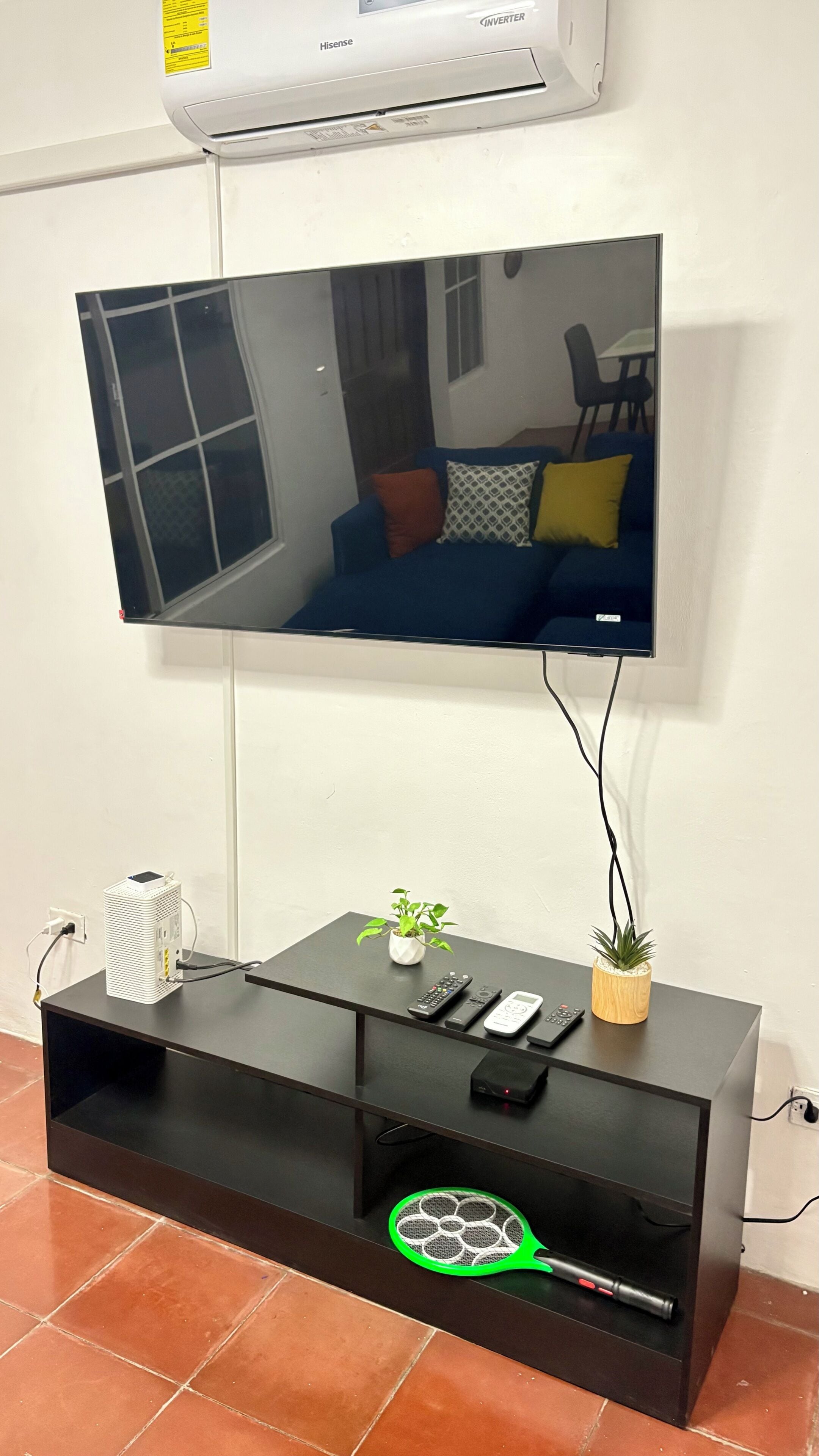 Un televisor de pantalla plana montado en una pared, un mueble de entretenimiento negro con una planta, y un aire acondicionado blanco.