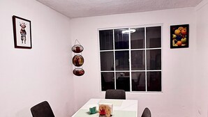 Ein Essbereich mit einem weißen Tisch, schwarzen Stühlen, einer Deckenleuchte und einem Fenster mit Jalousien.