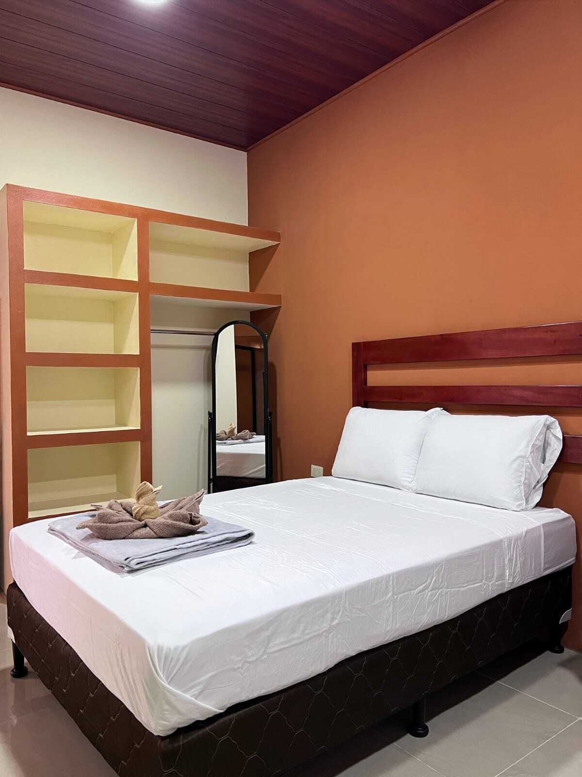 Quarto com cama, guarda-roupa com vários compartimentos, espelho e cabeceira de madeira.