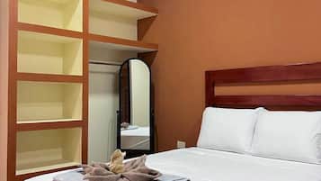 Une chambre d’hôtel comprenant un lit, une armoire avec plusieurs étagères, un miroir et une tête de lit.