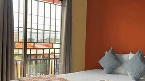 Hotellihuone, jossa on sänky, parveke, jolta on näkymä, ja ikkuna, jossa on verhot.