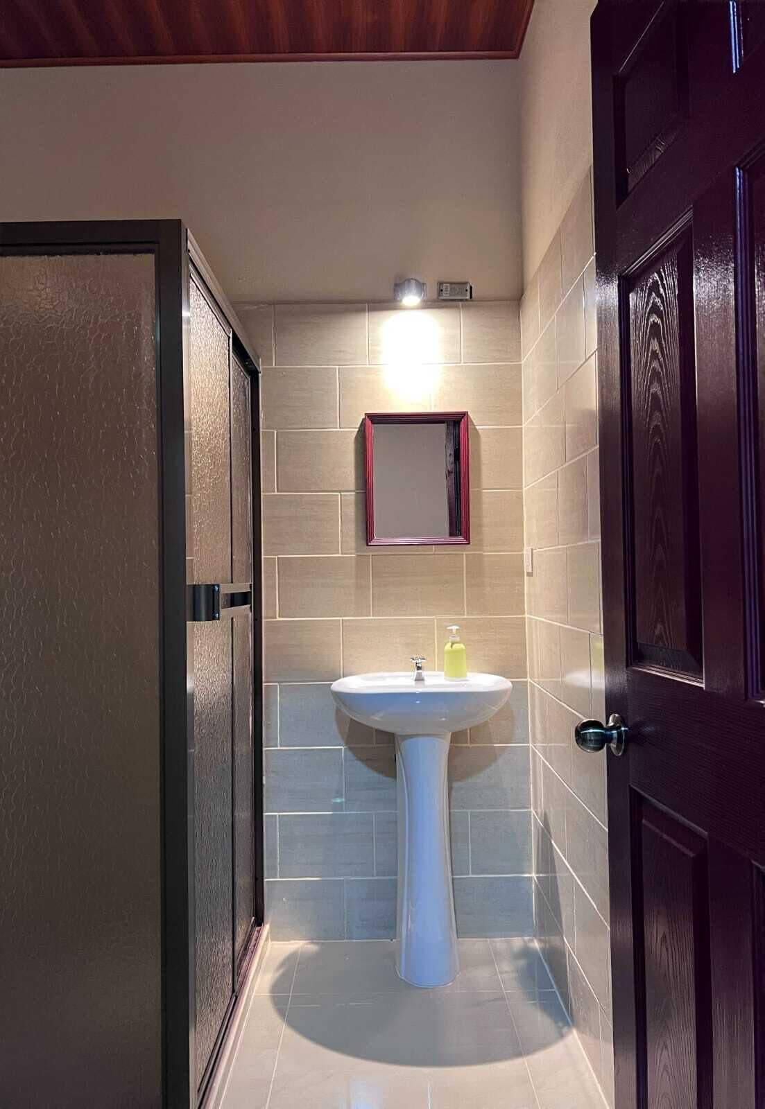 A bathroom with a pedestal sink, a mirror, and a door.