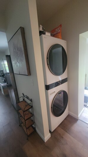 Une petite buanderie équipée d’un lave-linge et d’un sèche-linge à chargement frontal, d’un étendoir métallique et d’un tableau encadré accroché au mur.
