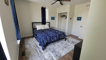 Ein Schlafzimmer mit Bett, Deckenventilator, Tür und einem Fenster mit Vorhängen.