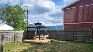 Un jardin avec une terrasse en bois, un kiosque et un bâtiment rouge.