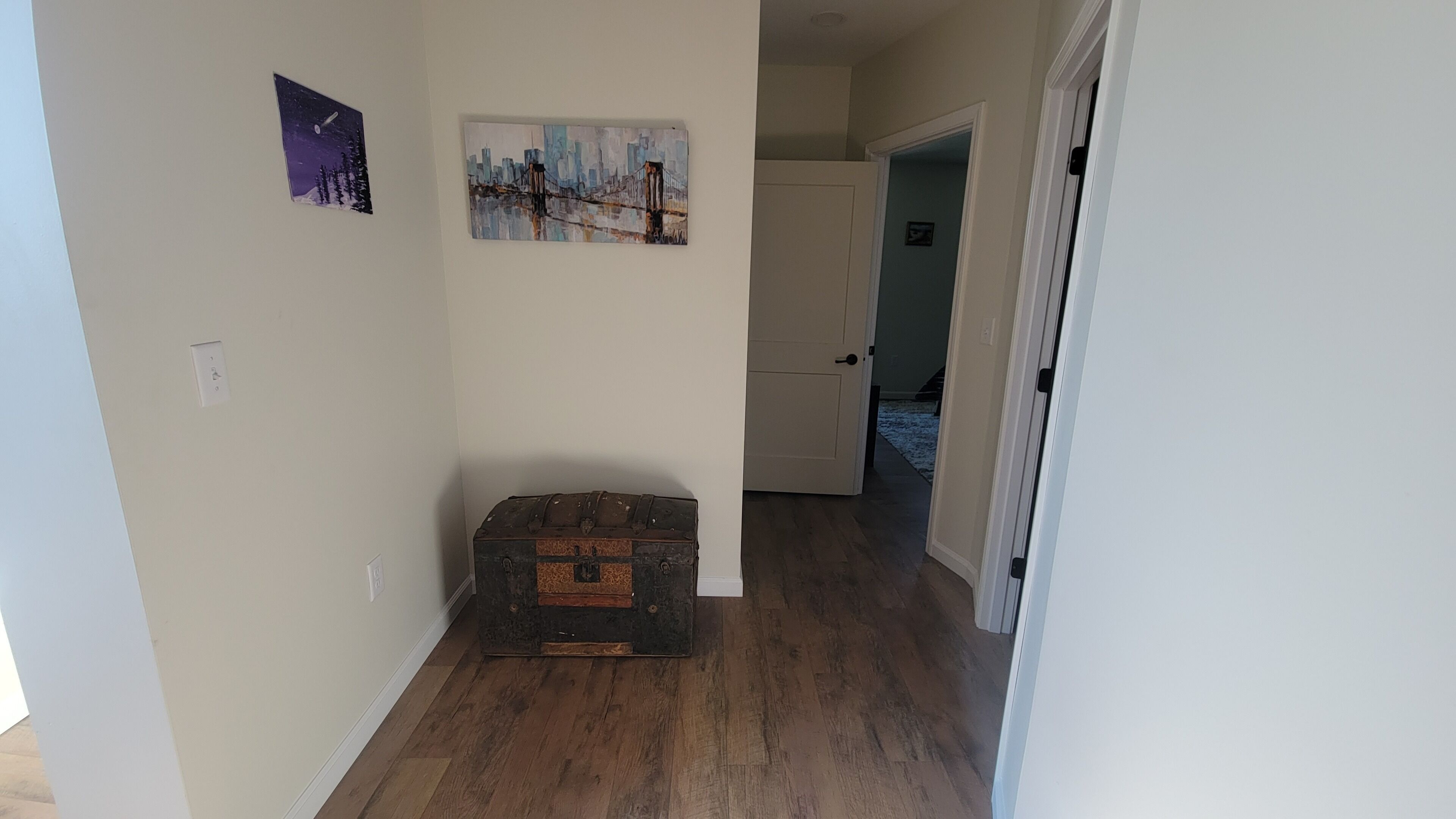 A hallway with wooden flooring, a vintage suitcase, and two wall-mounted paintings.