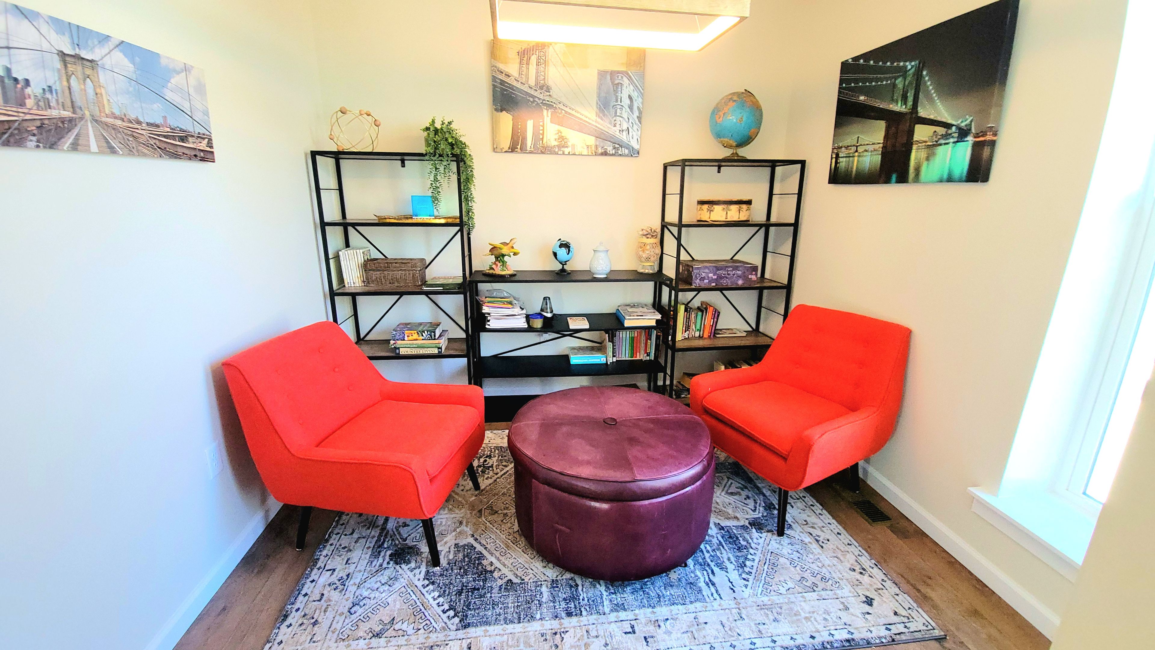 Una habitación con dos sillas rojas, un reposapiés morado, una estantería y un globo terráqueo.