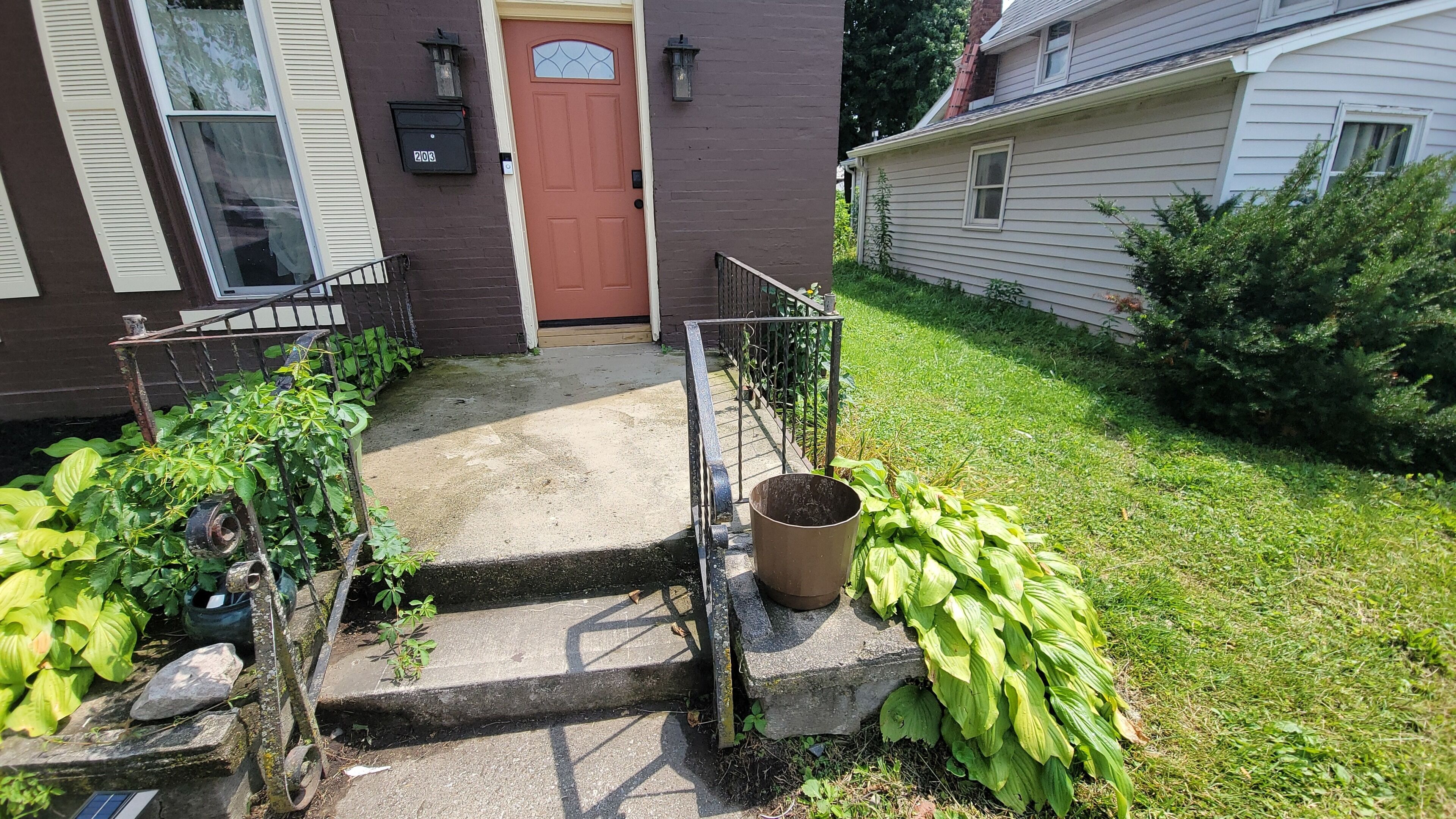 A front yard with a concrete staircase leading to a brown door, a metal gate, and a potted plant.