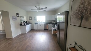 Una cucina con mobili bianchi, lavastoviglie, frigorifero e ventilatore a soffitto.