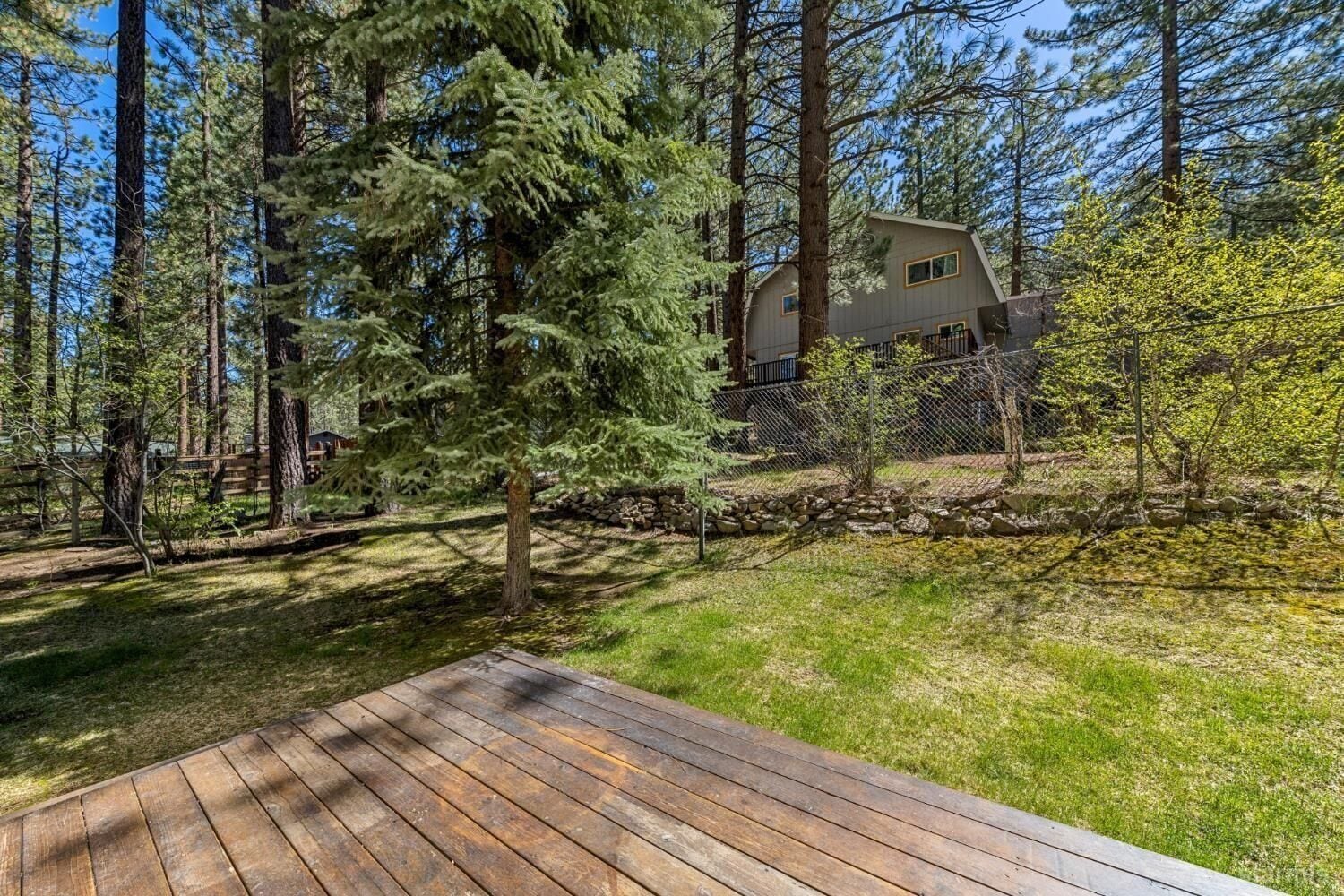 Propiedad residencial con terraza de madera, rodeada de árboles altos y un muro de piedra.