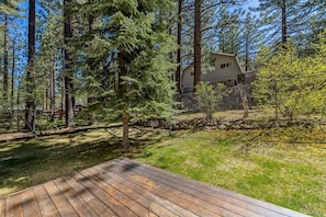 A residential property with a wooden deck, surrounded by tall trees and a stone wall. - Classic A-Frame Cabin Near Heavenly Resort | Cozy South Lake Tahoe Vacation Real (South Lake Tahoe)