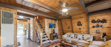 A wooden interior with a staircase, a sofa set, and a ceiling fan.