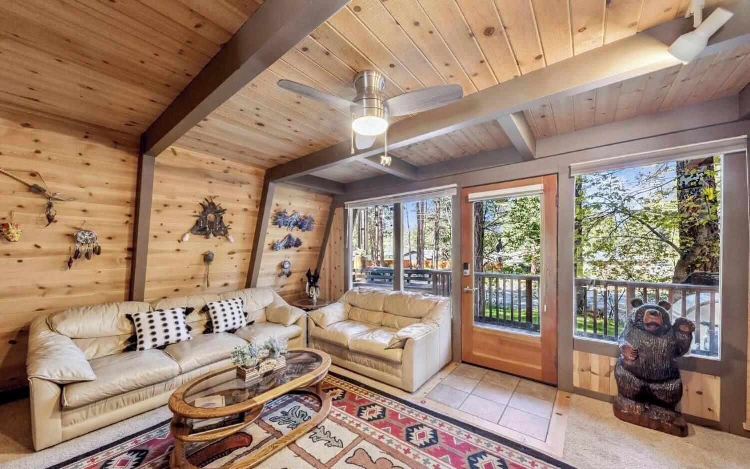 A cozy cabin interior with two sofas, a ceiling fan, and a bear statue by the door.