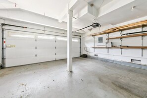 Een garage met twee witte garage deuren, een betonnen vloer en metalen schappen aan de rechtermuur.