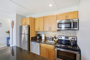 A modern kitchen with stainless steel appliances, wooden cabinets, and a granite countertop. - NEW- Renovated Ocean view- Across from the beach- Fantastic location (Kihei)