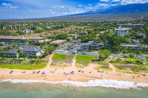 Un poble costaner amb una platja, edificis i una muntanya al fons.