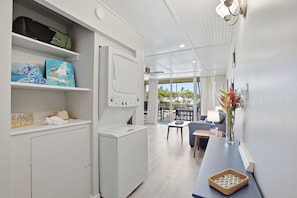 A modern kitchen with a built-in washer and dryer, a dining area with a view, and a small table with a vase of flowers. - NEW- Renovated Ocean view- Across from the beach- Fantastic location (Kihei)