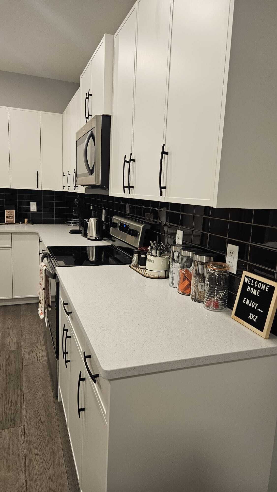 A modern kitchen with white cabinets, a black tiled backsplash, and a stainless steel range hood.