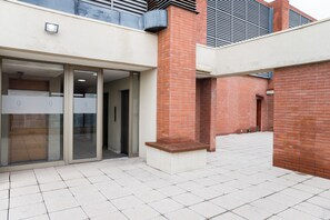 A building entrance with a glass door, a brick wall, and a tiled floor. - Americo Vespucio Apartments By Andes STR (Las Condes)