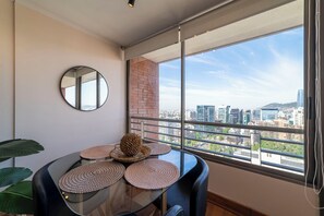 Ein Essbereich mit einem Glastisch, gewobenen Platzsets und Blick auf die Stadt durch große Fenster.