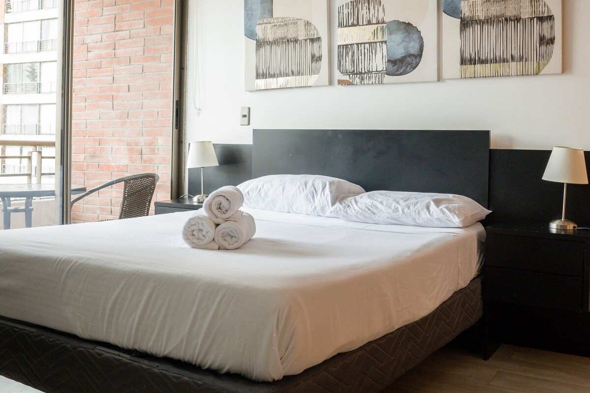 A modern bedroom with a large bed, a brick wall, and three abstract wall art pieces.
