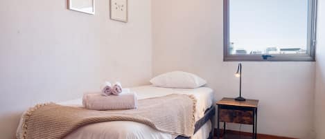 A bedroom with a bed, a bedside table with a lamp, a window with a view, and two framed pictures on the wall.