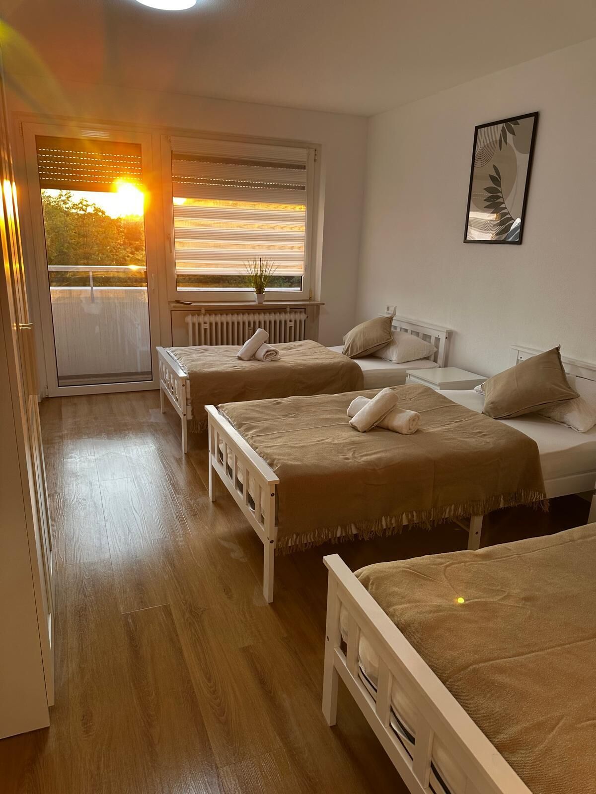 Habitación con tres camas, un radiador, una ventana con persianas y una planta.