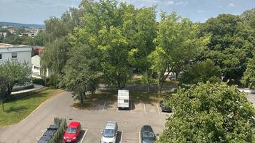 Ein Parkplatz mit mehreren Autos und einem weißen Lieferwagen, umgeben von Bäumen und einem Gebäude im Hintergrund.