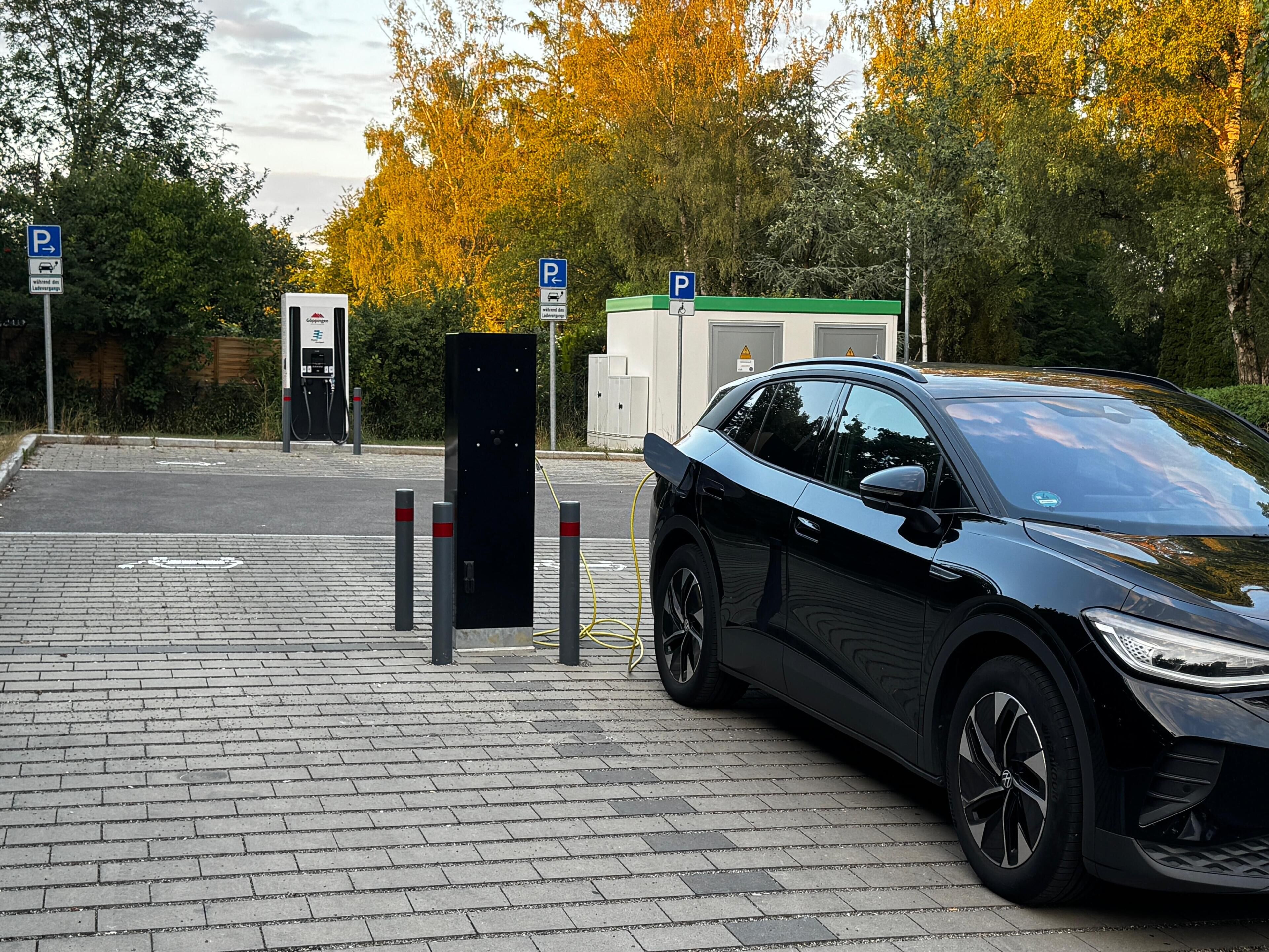 A parking area with electric vehicle charging stations, a car, and a building with a green roof.