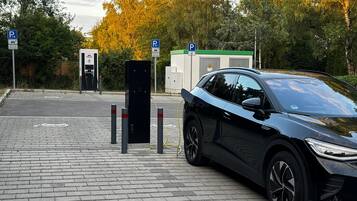 A parking area with electric vehicle charging stations, a car, and a building with a green roof.