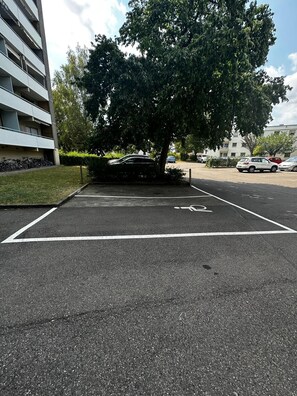 Un área de estacionamiento con un símbolo de bicicleta, un árbol y un edificio con balcones.