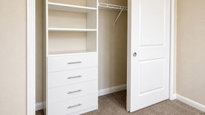 A walk-in closet with open doors, featuring a white wardrobe with multiple drawers and shelves, and a hanging rod. - Tempo Room Lodgings (Kissimmee)