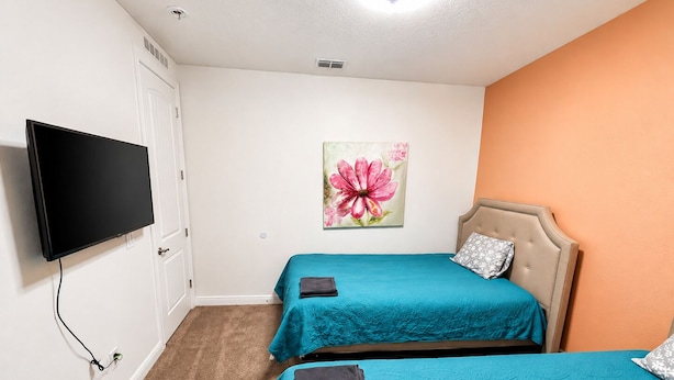 A hotel room with two beds, a television, a painting, and a carpeted floor. - Tempo Room Lodgings (Kissimmee)
