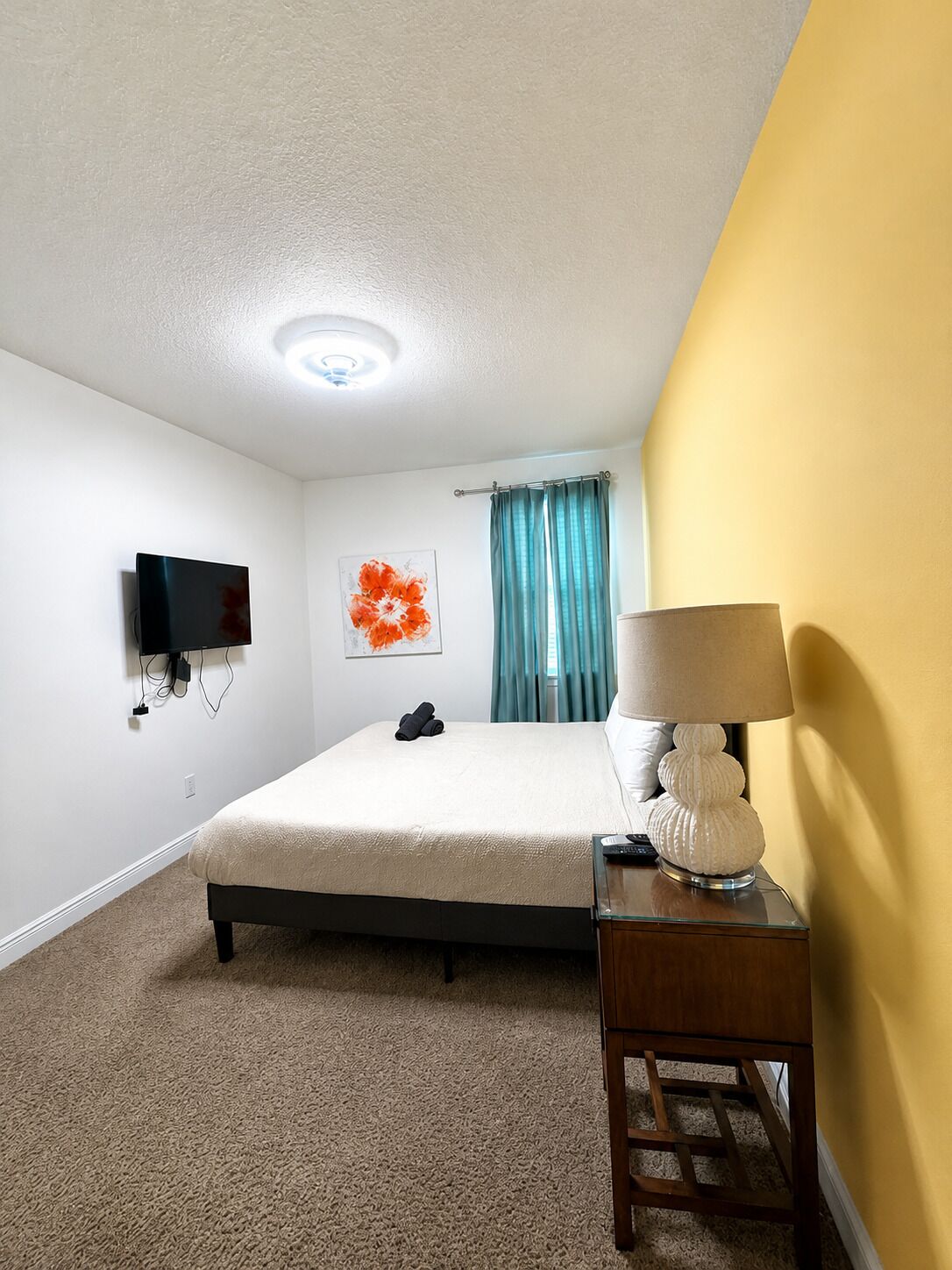 Een hotelkamer met een bed, een flatscreen televisie aan de muur, een nachtkastje met een lamp en een raam met gordijnen.