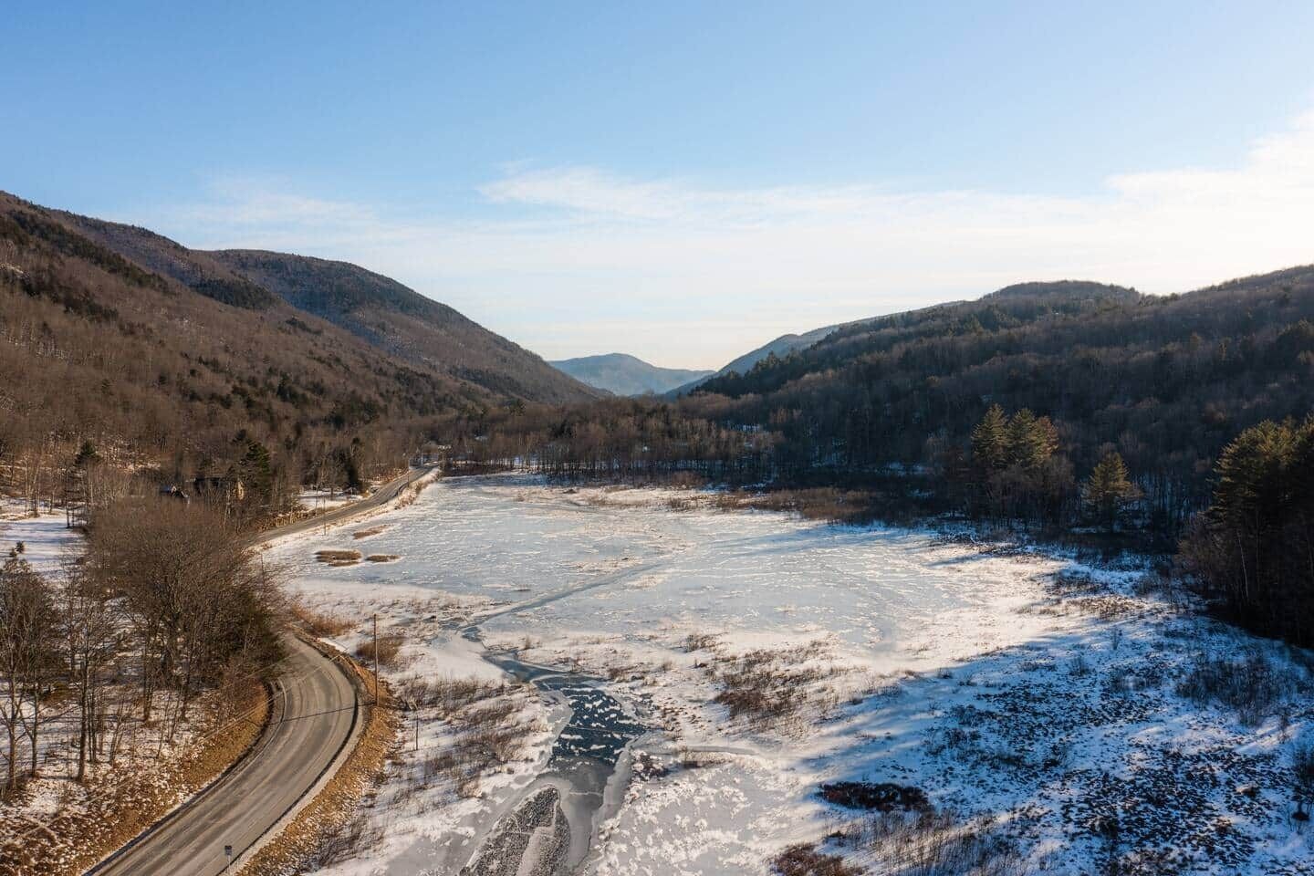 Ein gefrorener Fluss mit einer sich schlängelnden Straße parallel dazu, umgeben von bewaldeten Hügeln.
