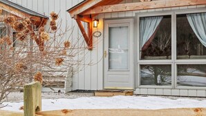 Une cabane en bois, le sol recouvert de neige, une clôture en bois et une porte surmontée d’une fenêtre.