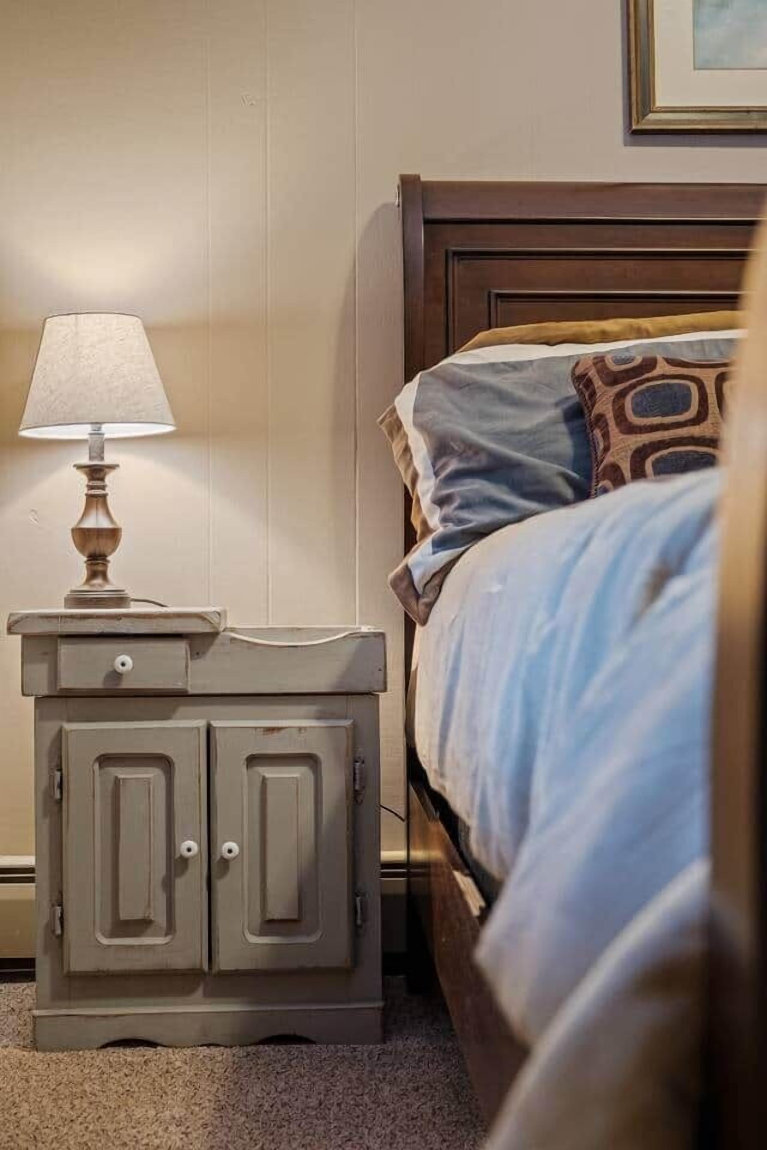 Une chambre à coucher avec une tête de lit en bois, une table de chevet avec une lampe et un lit recouvert d’une literie à motifs.