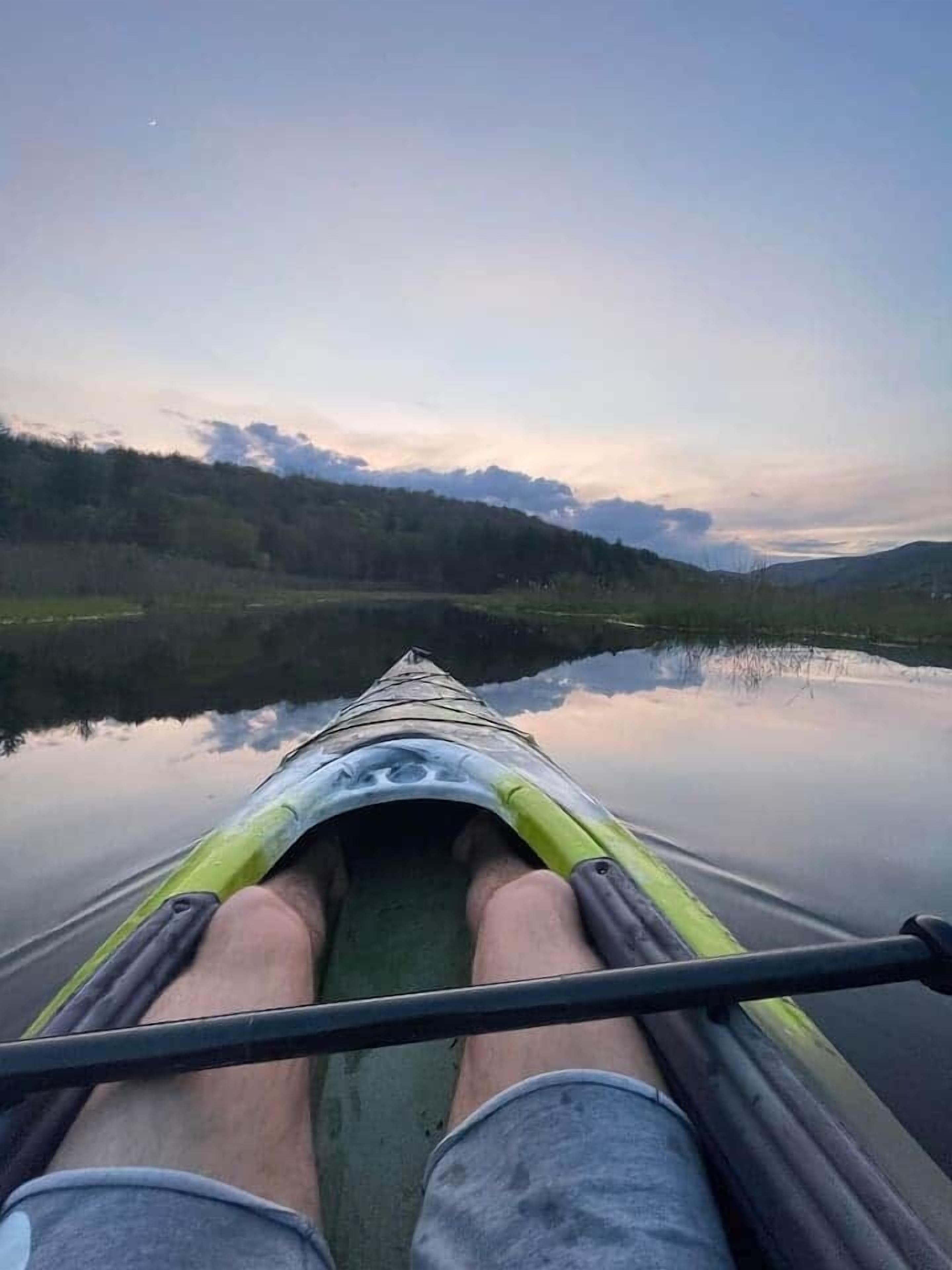 Ein Kajak auf einem ruhigen See vor einer bewaldeten Landschaft.