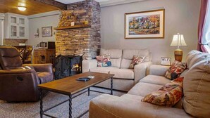 Un salon chaleureux avec une cheminée en pierre, un canapé, un fauteuil inclinable et une table basse.