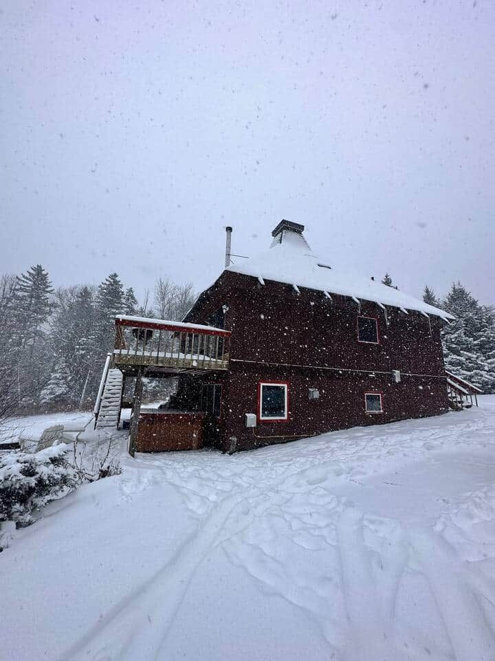 Una baita di legno ricoperta di neve con un balcone, circondata da alberi innevati.