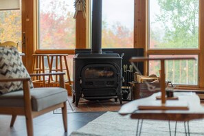 Ein gemütliches Wohnzimmer mit Kaminofen, Holzmöbeln und großen Fenstern.