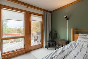 Ein Schlafzimmer mit einem Bett, einem Sessel, einem Nachttisch, einer Lampe und einer Schiebetür zu einer Terrasse.