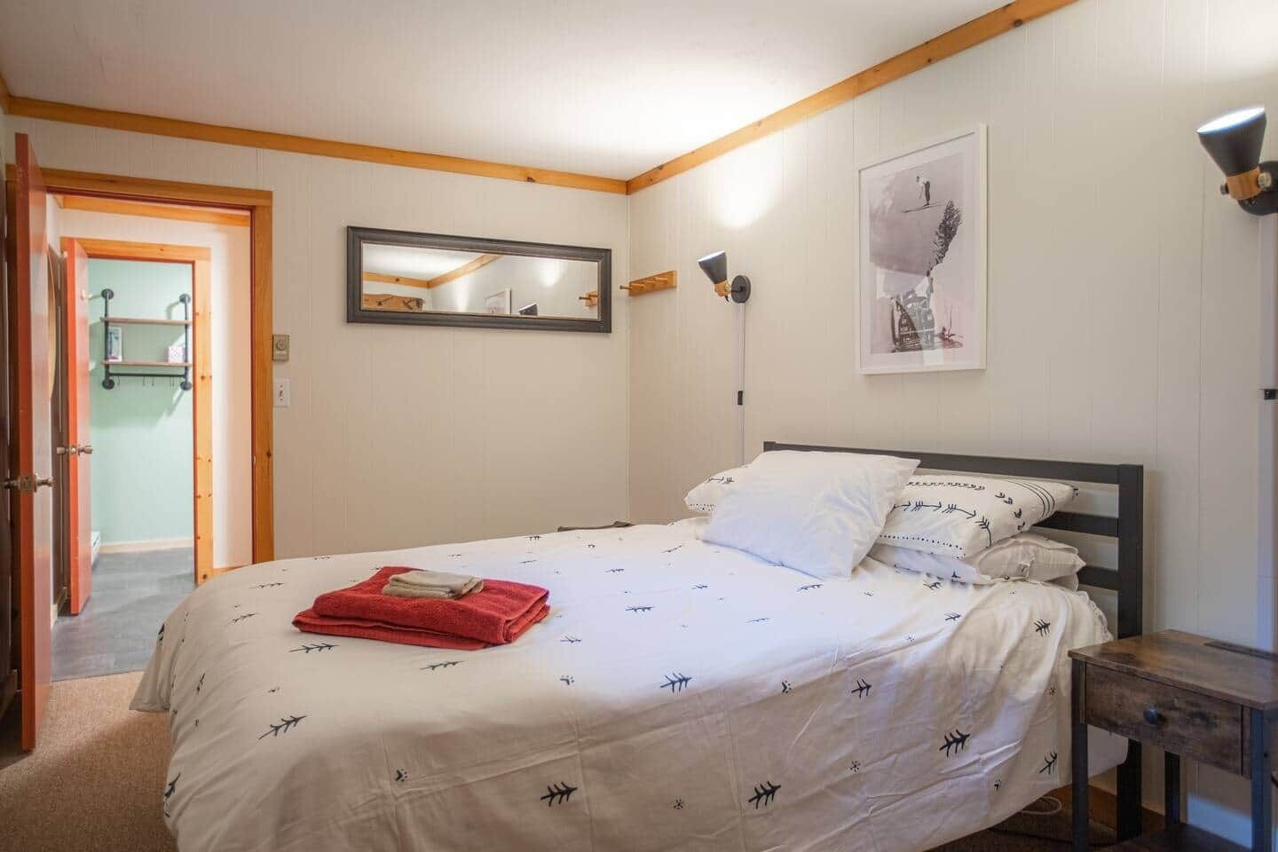 Une chambre à coucher comprenant un lit, une table de chevet, un miroir et un luminaire fixé au mur.