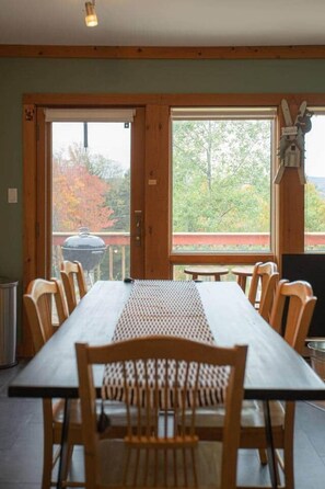 A dining area with a long table and chairs, large windows with a view of trees, and a barbecue grill outside. - MtSnow* HotTub*  Pool * AirHockey*PingPong * Darts (Wilmington)