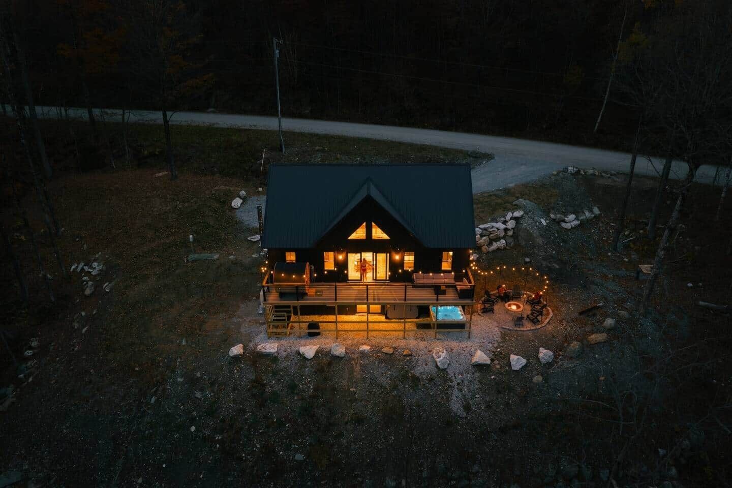 A cabin with a dark roof, a deck with outdoor seating, and a fire pit.