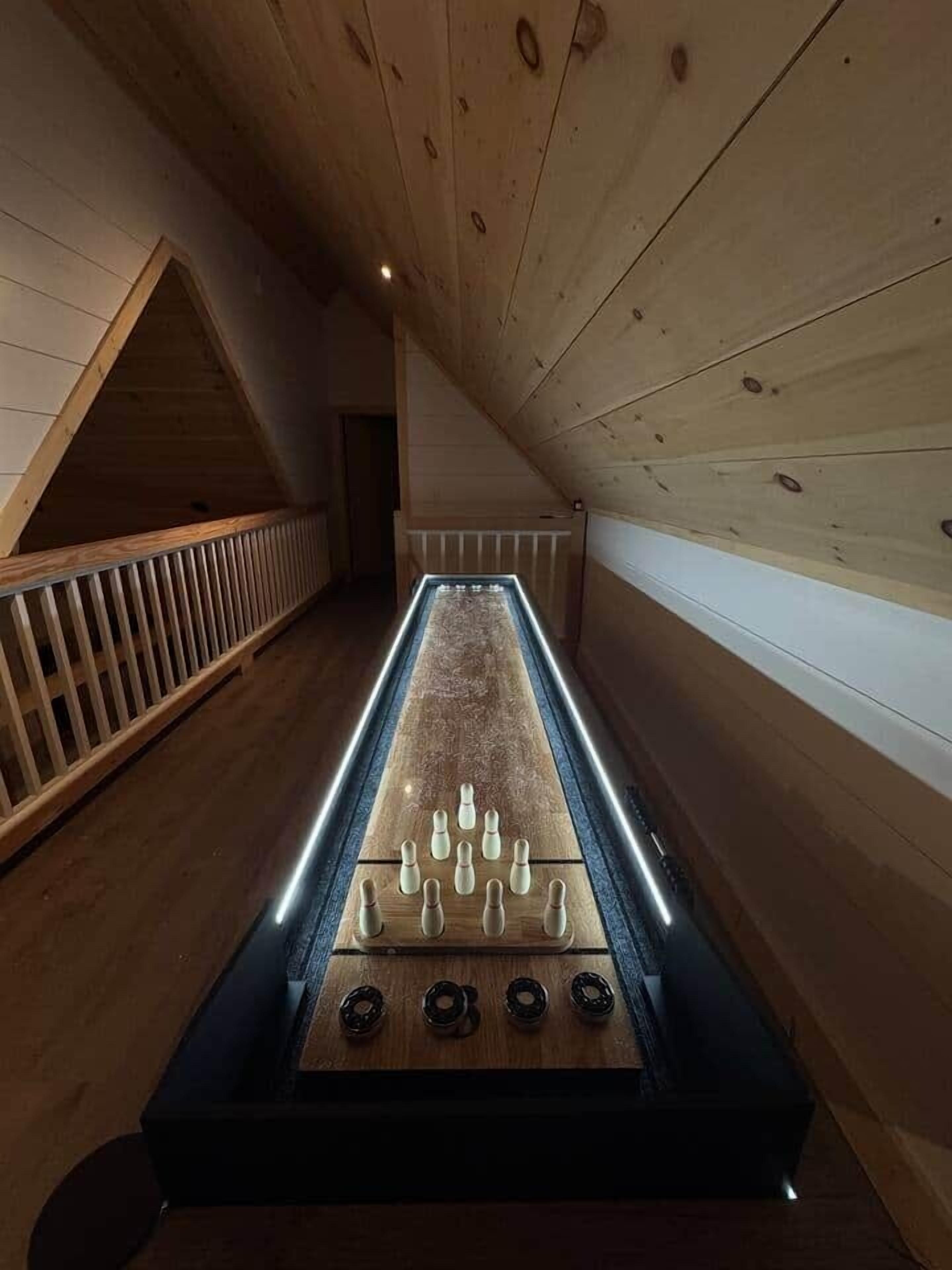 A room with a long, narrow foosball table, wooden walls, and a sloped ceiling.