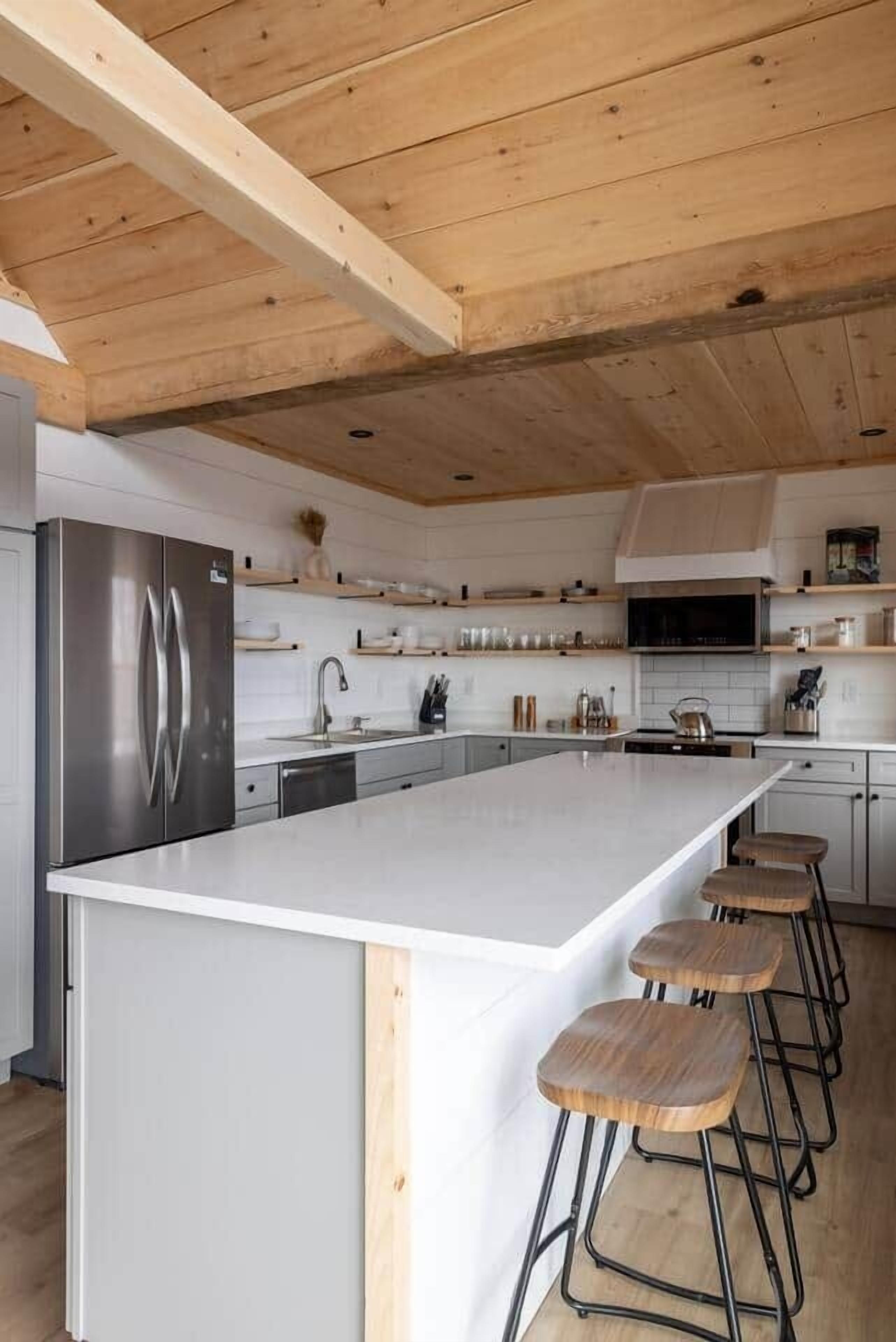 A modern kitchen with a large island, stainless steel appliances, and wooden bar stools.